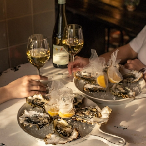 Two individuals enjoying wine and oysters, a perfect pairing for a delightful evening.