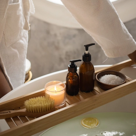 Person in bathtub holding wooden tray with Wellness items