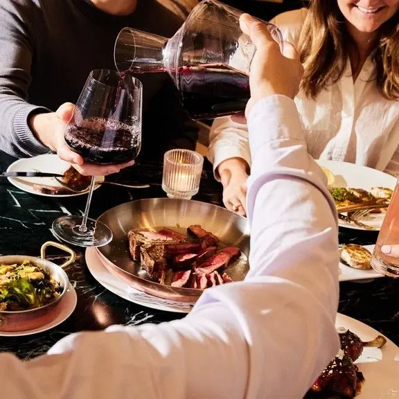 A group of people enjoying a meal at a restaurant, holding wine glasses and engaging in conversation.