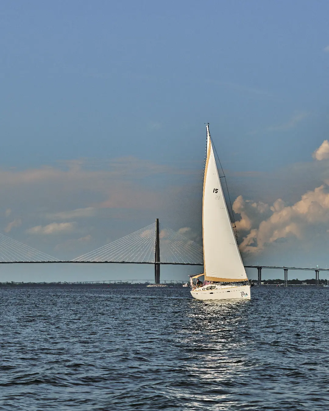 Serenely sailing amidst the endless ocean, a sailboat graces the scene, accompanied by a picturesque bridge in the distance.